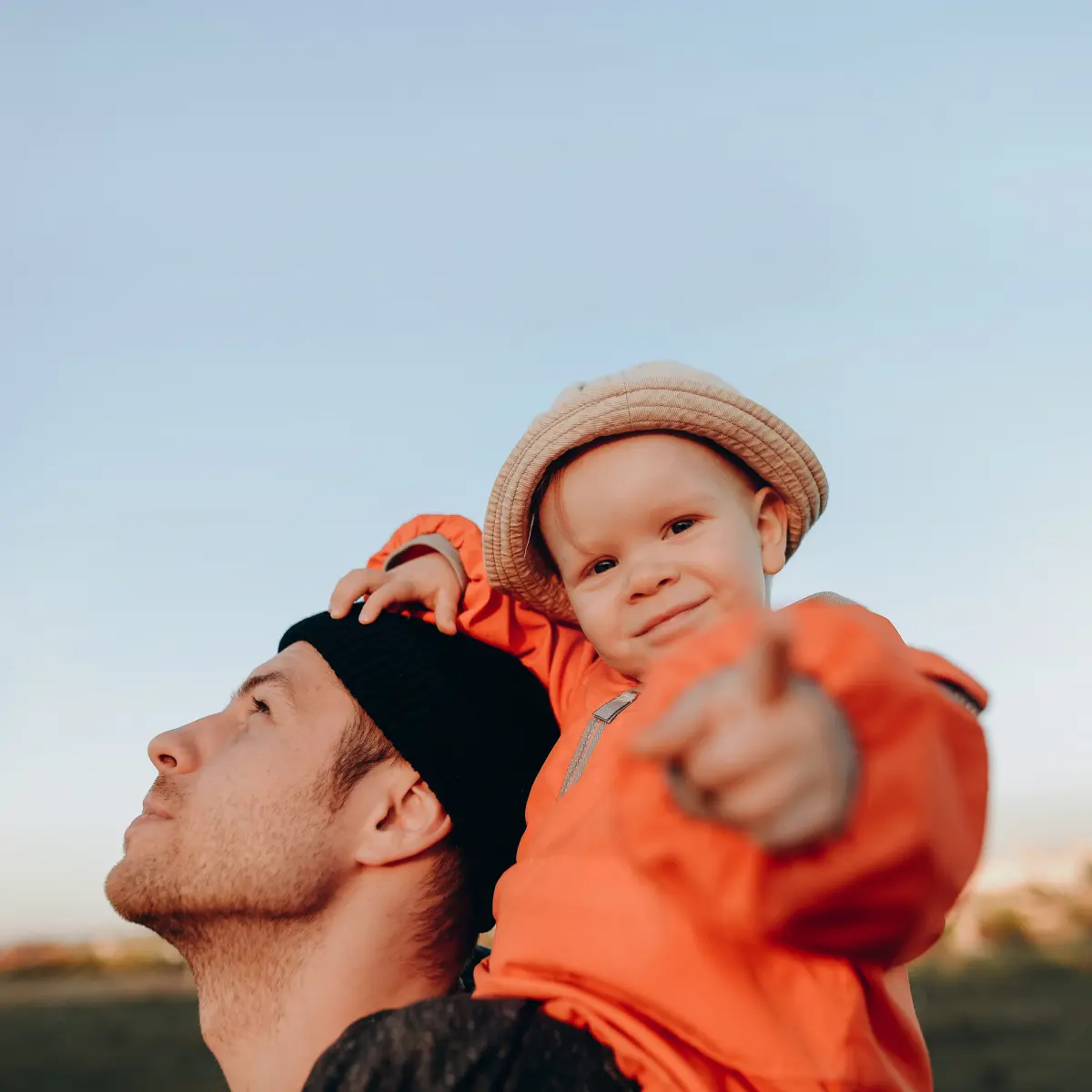 raisin_de_vater_kind_zukunft.png Vater umarmt zwei fröhlich lachende Kinder vor grauem Hintergrund.