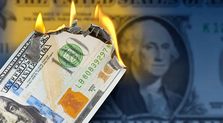 Billetes de cien dólares en llamas con primer plano de la cara de Washington desenfocado.