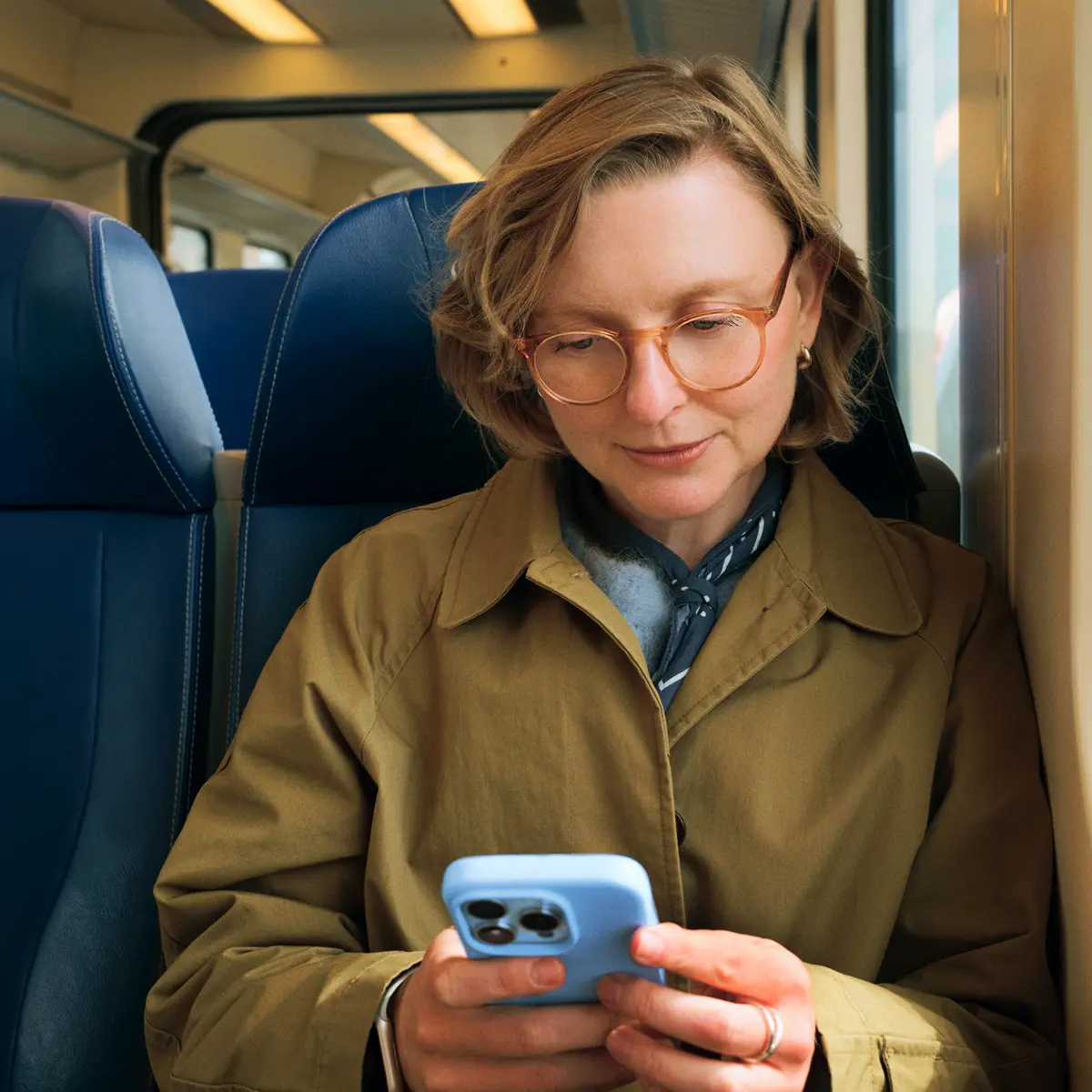 raisin_de_frau_zug_portfolio_app.png Mann blickt lächelnd in die Kamera, während er ein Smartphone vor einem Fenster hält.