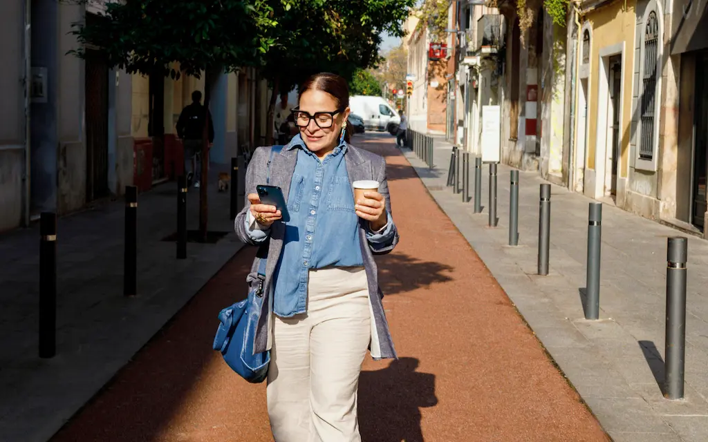 stocksy-7126588-Raisin_IT_Teaser.png Donna che cammina per strada con telefono e caffè in mano