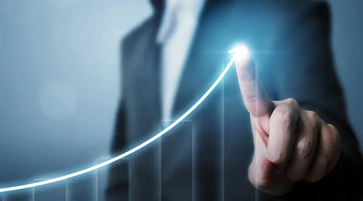 Een hand wijst op een gloeiende, stijgende lijn in een grafiek, met vaag een zakenman op de achtergrond, wat groei symboliseert.
