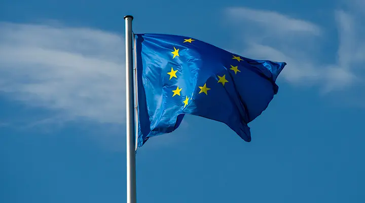 Bandera azul con estrellas amarillas ondea con gran símbolo del euro en el centro.