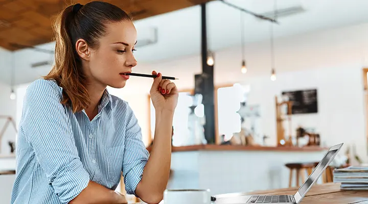 Persona reflexiona apoyando el bolígrafo en la barbilla ante un ordenador en una oficina.