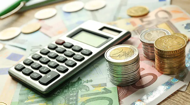 Rekenmachine ligt op eurobankbiljetten naast diverse stapels munten.