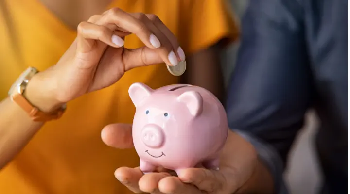 Una mano mete un euro en una hucha con forma de cerdo.