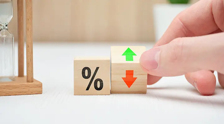 Mano sostiene bloque con un % y flechas verde hacia arriba y roja hacia abajo para indicar cambios en tasas.