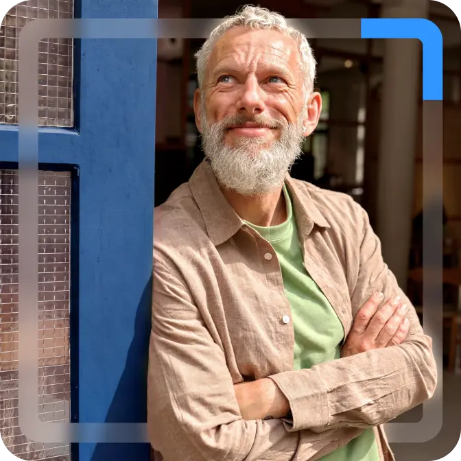 raisin-uk-hero-man-looking-into-distance.png A man with a grey beard and a beige shirt looks into the distance with his arms folded, smiling