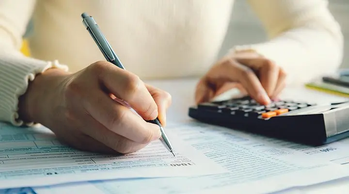 Iemand schrijft met een pen op papier, met een rekenmachine ernaast.