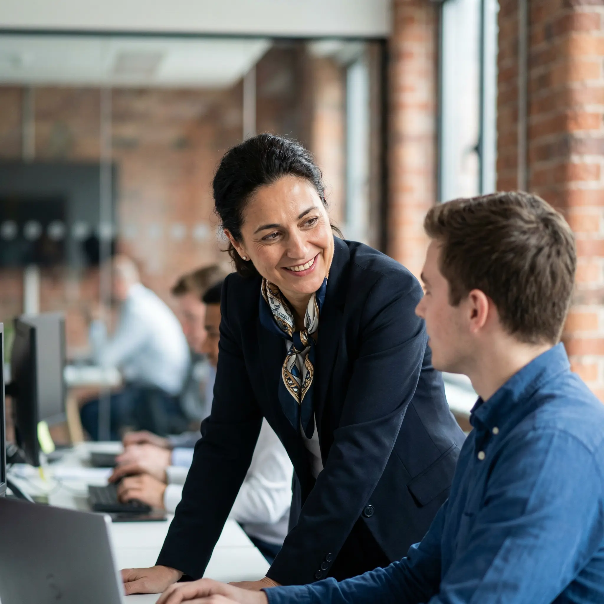 About-Alpine-Capital-Bank.png Woman smiling and speaking with a colleague in a modern office
