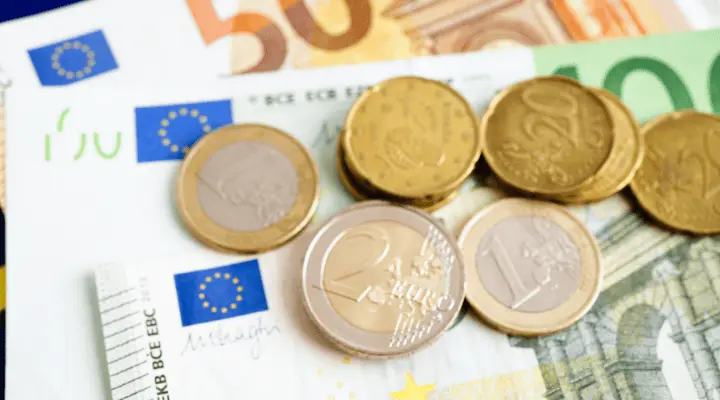 Monedas de distintos valores apiladas sobre billetes de euro en mesa.