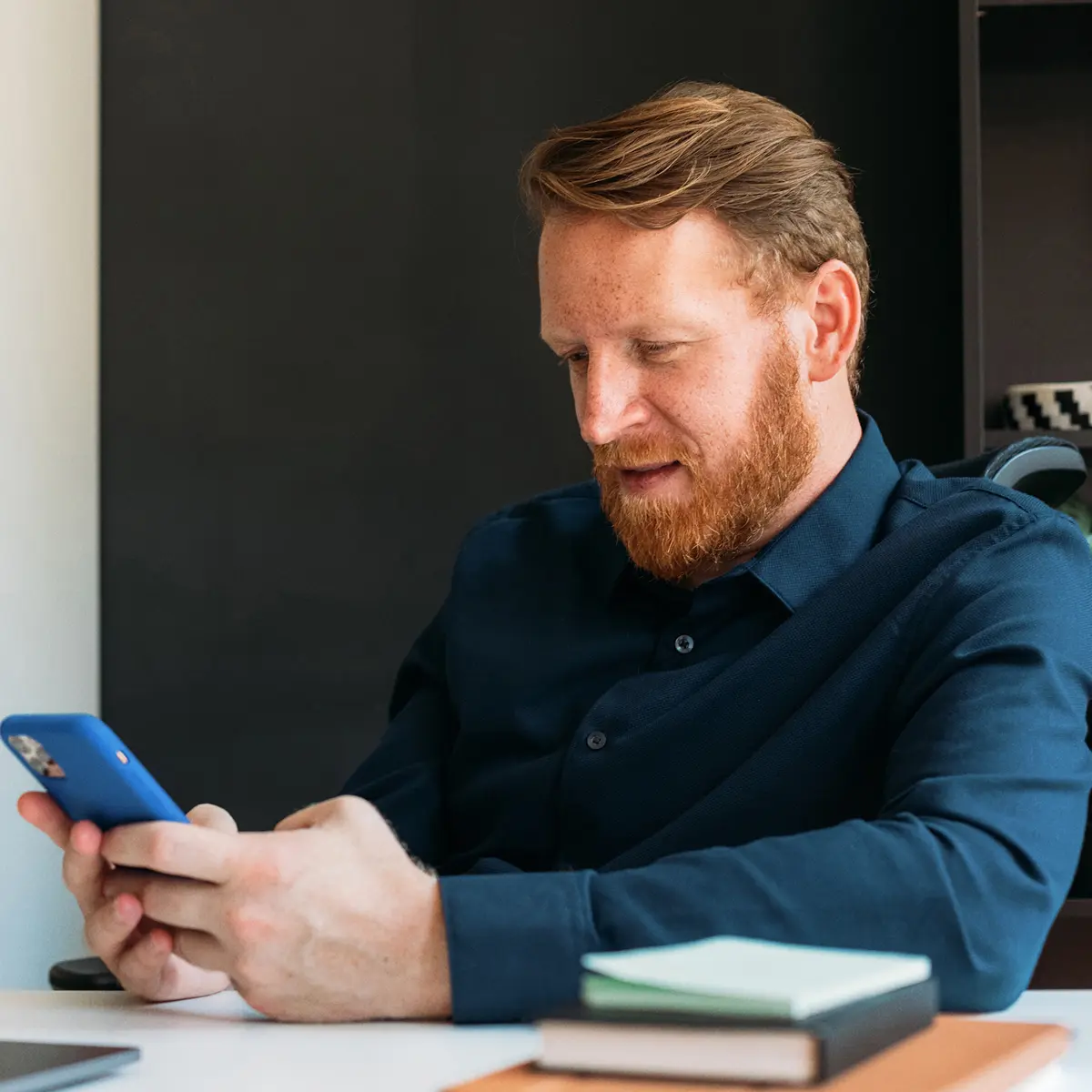 raisin_de_mann_smartphone_online_banking.png Mann im Hemd sitzt am Schreibtisch und nutzt sein Smartphone für Online-Banking.