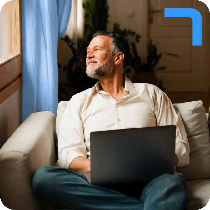 A bearded man in a cream-coloured shirt types on a laptop, while looking out of a sunlit window