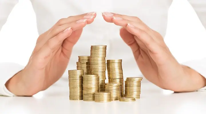 Bild von mehren Münzstapeln sowie zwei Händen welche in einer schützenden Form über die Münzen gehalten werden.