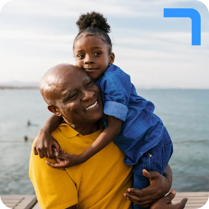 raisin-uk-man-with-daughter.png A man in a yellow polo shirt holding his daughter, who is wearing a blue denim shirt and jeans