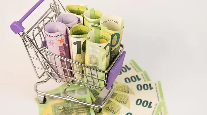 Miniatuur winkelwagen gevuld met opgerolde eurobankbiljetten