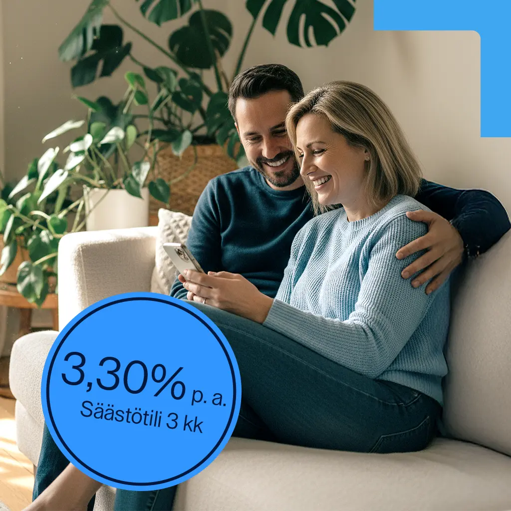A man and a woman sit on a couch, smiling as they look at their smartphones