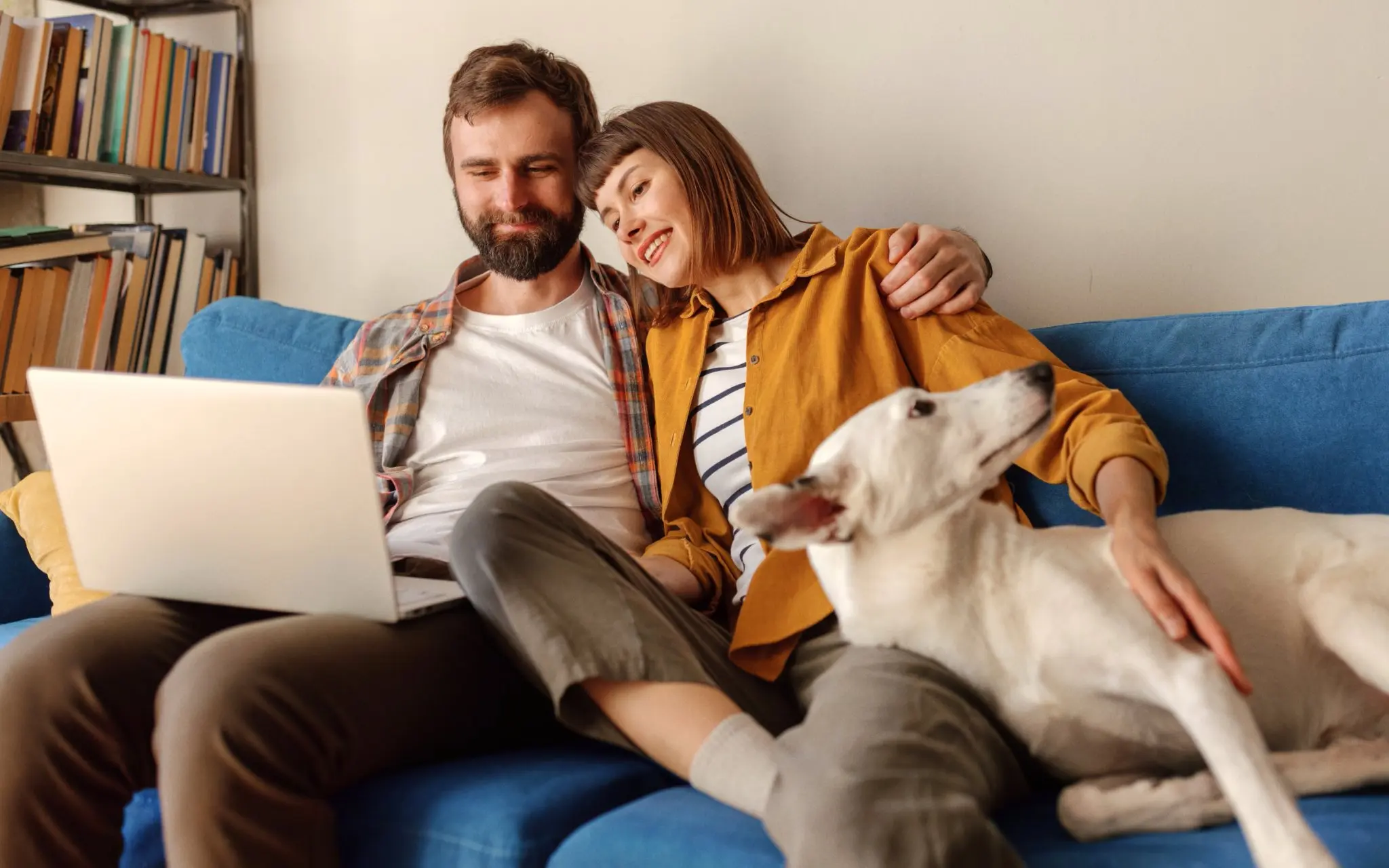 stocksy-5415744-edit-weblayer.jpg A man and a woman sit on a sofa looking at a laptop together with their dog next to them.