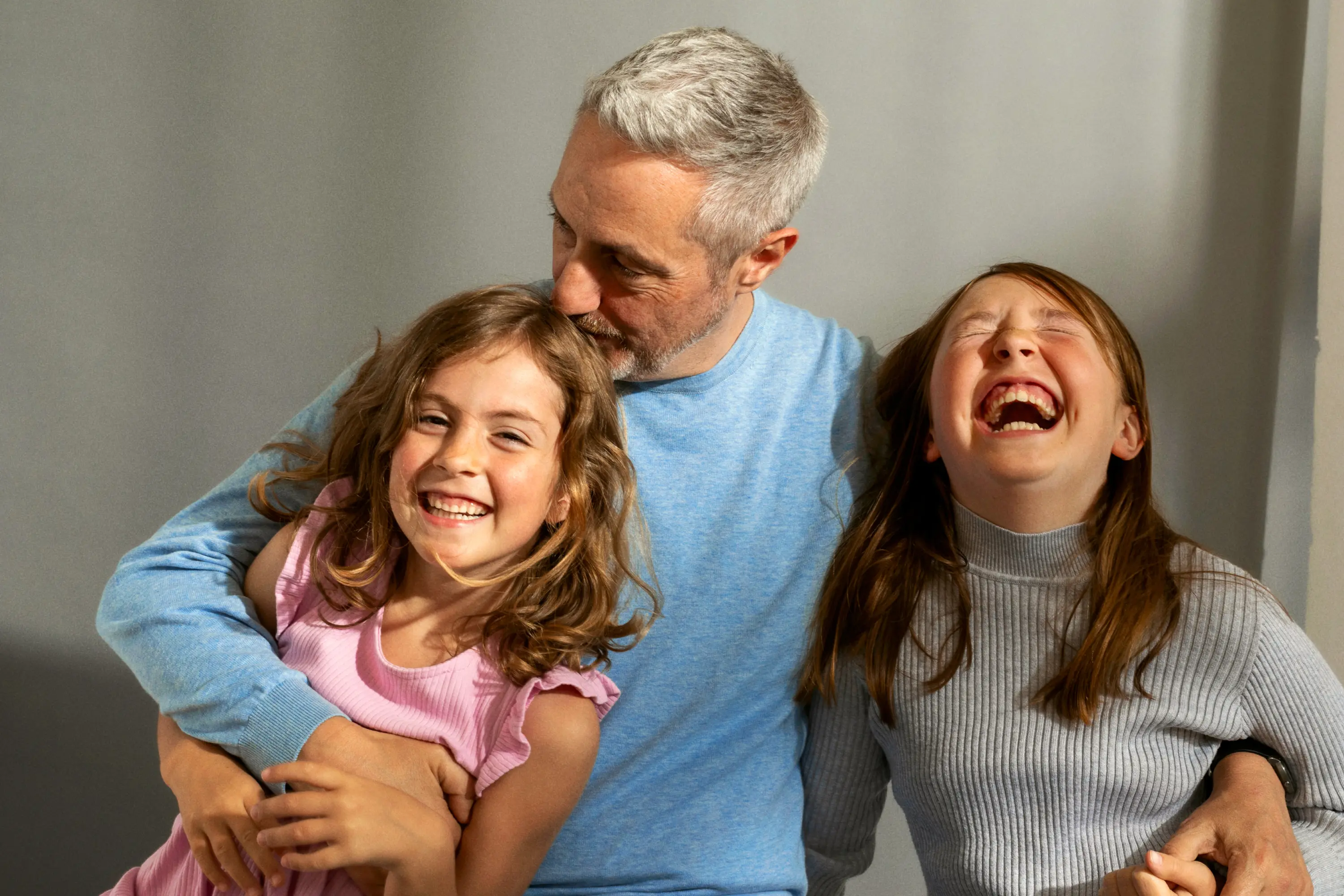 Ein lachender Vater umarmt seine zwei glücklichen Töchter herzlich.