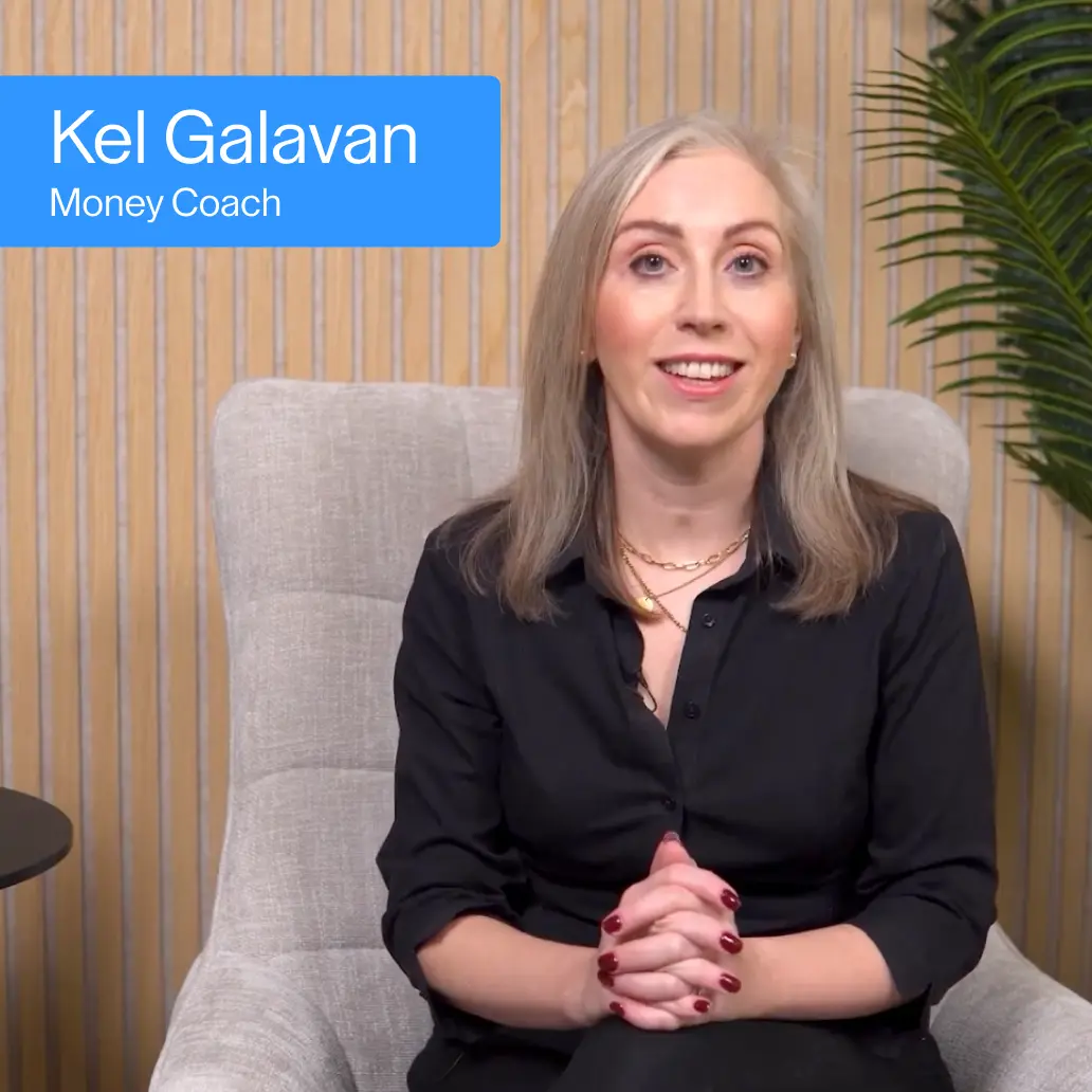 Kel Galavan, Money Coach, seated in a chair against a wood panel backdrop, smiling at camera.