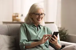 Woman sitting on couch and smiling while she looks at her cell phone
