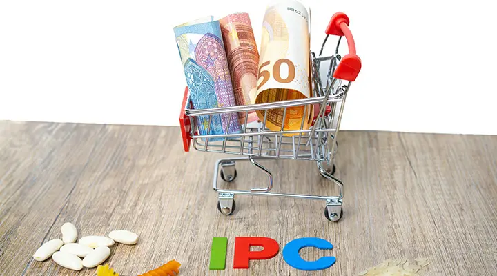 Carrito metálico pequeño con billetes y monedas de euro sobre mesa de madera.