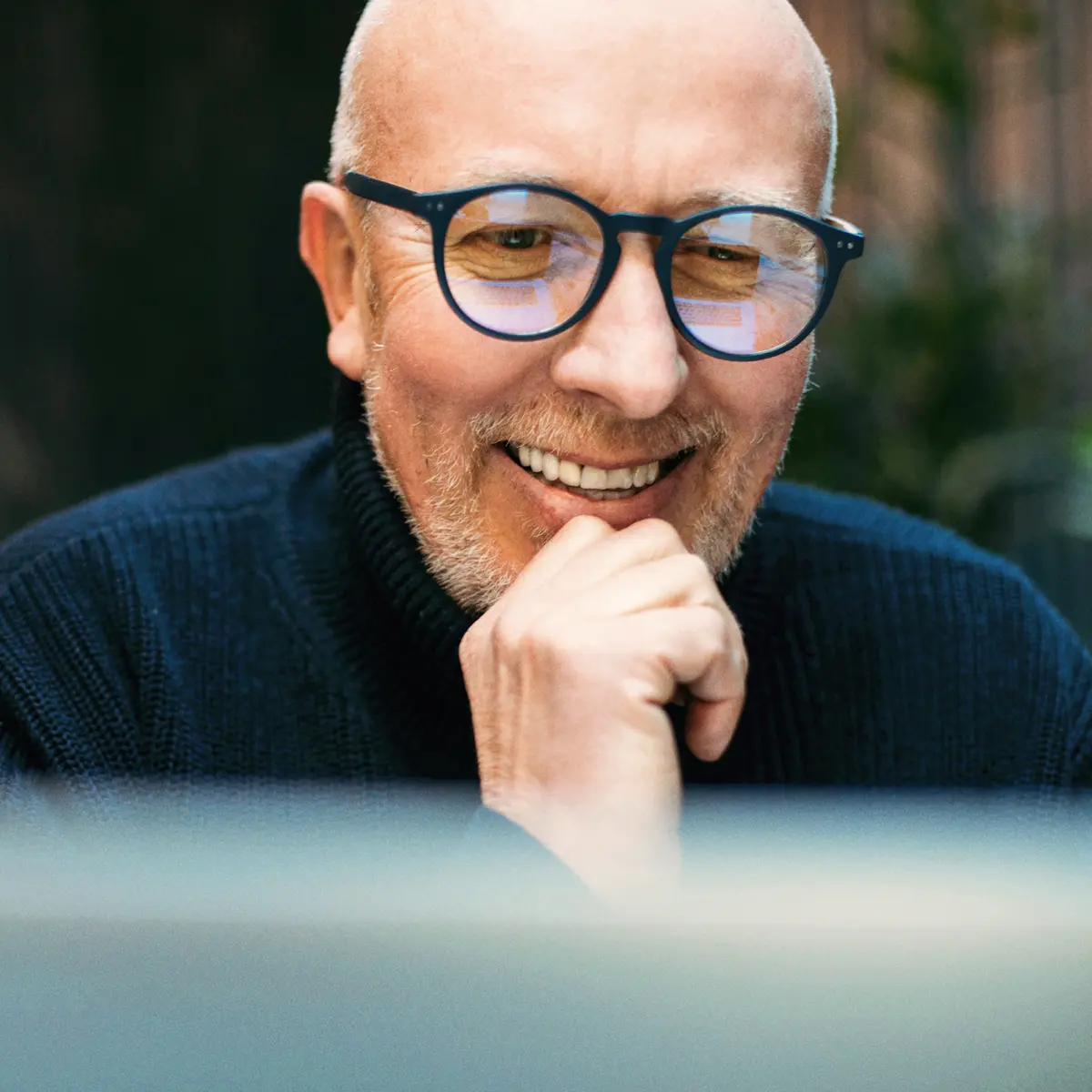 Raisin DE-senior_brille_altersvorsorge.jpg Lächelnder älterer Mann mit Brille blickt zufrieden auf einen Bildschirm.