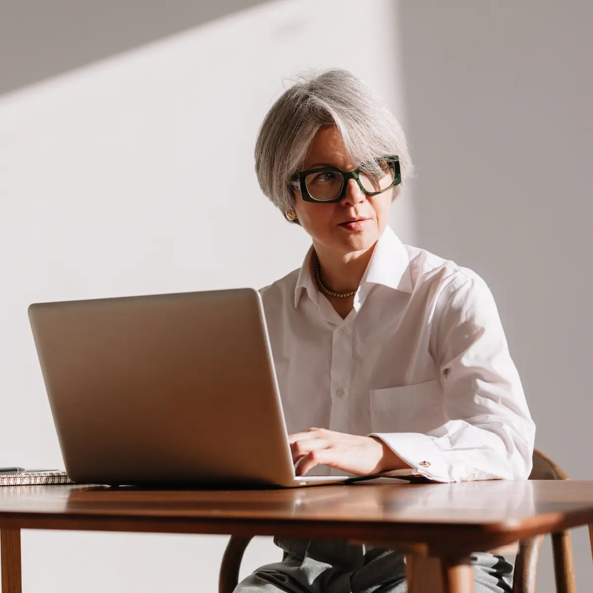 Raisin DE-frau_laptop_arbeit_buero Geschäftsfrau mit Brille arbeitet konzentriert am Laptop an einem Holztisch bei Tageslicht.