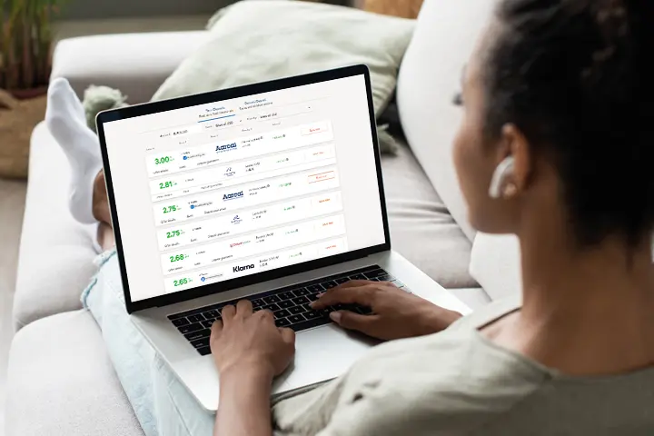 Woman sitting on a couch using a laptop, viewing the Raisin savings account comparison table on the screen.
