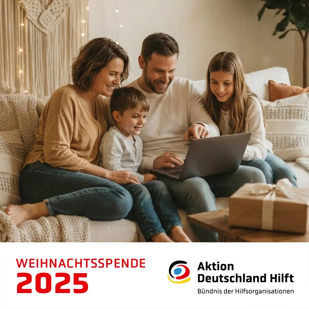 Raisin DE kunden werben Aktion Deutschland Hilft Eine vierköpfige Familie sitzt gemütlich auf einem Sofa und schaut gemeinsam auf einen Laptop. Im Vordergrund stehen drei brennende Kerzen auf einem Holztisch. Unten im Bild befindet sich ein weißer Bereich mit roter Aufschrift ‚Weihnachtsspende 2025‘ sowie dem Logo von ‚Aktion Deutschland Hilft – Bündnis der Hilfsorganisationen‘.