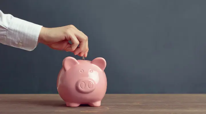 Mano mete una moneda en hucha con forma de cerdo.