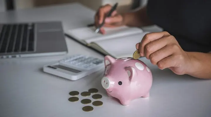 Persona metiendo moneda en hucha de cerdo.