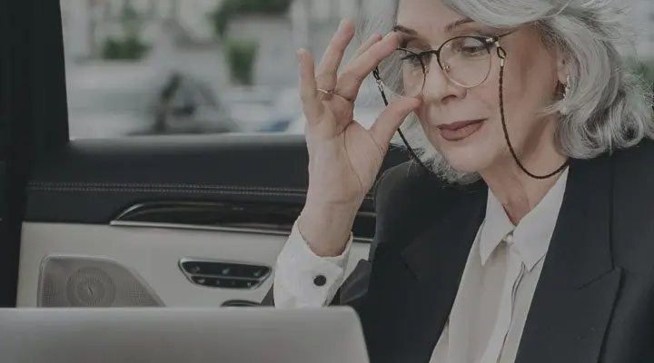 Mujer madura con gafas ajusta montura frente a un portátil en un vehículo.