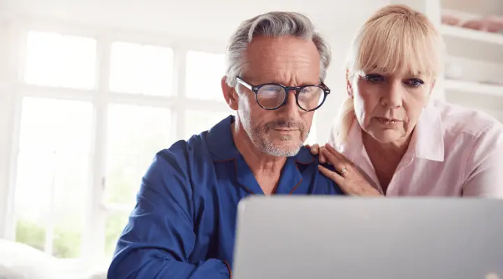 Een ouder stel buigt zich samen over een laptop, geconcentreerd kijkend naar het scherm.