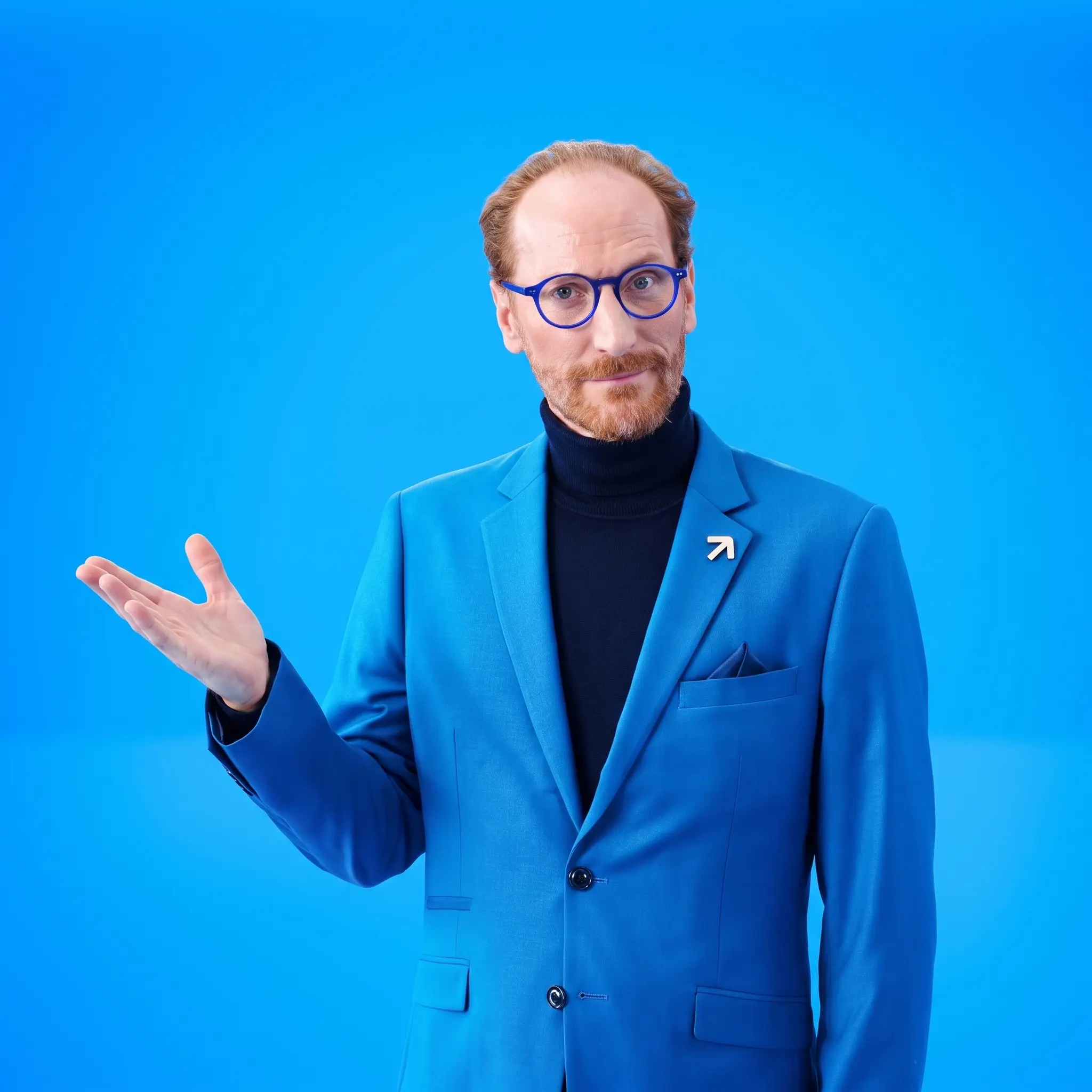 Man wearing a blue suit and glasses gesturing with an open palm against a solid blue background.